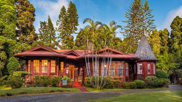 A traditional red-roofed building with a conical roof, surrounded by lush greenery and tall trees. - Comfortable Room in Historic Bed and Breakfast (Volcano)