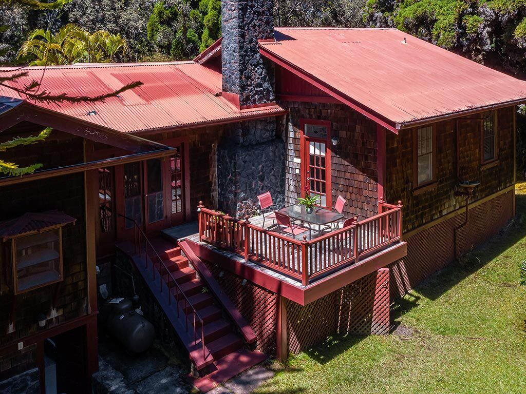 A two-story cabin with a red roof, a balcony with red railings, and a stone chimney.