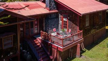 A two-story cabin with a red roof, a balcony with red railings, and a stone chimney.