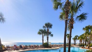 A clear blue swimming pool with a curved edge, surrounded by palm trees and lounge chairs. - AQUA 1509 — Luxury Oceanfront Condo• 3 BD• Steps to Pier Park (Panama City Beach)