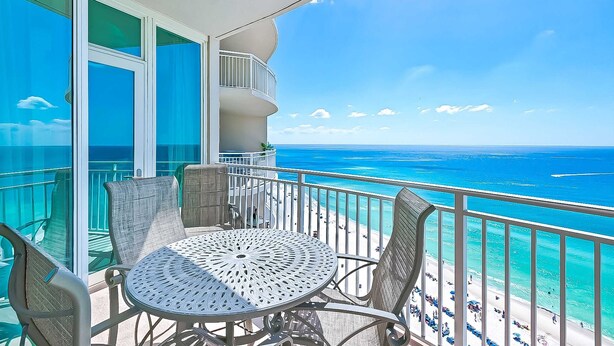 A balcony with a round table and chairs, overlooking a beach with clear blue water and a bright sky. - AQUA 1509 — Luxury Oceanfront Condo• 3 BD• Steps to Pier Park (Panama City Beach)