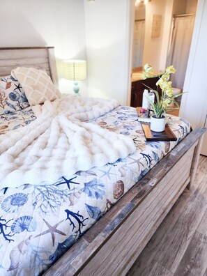 A bed with a nautical-themed duvet, a small potted plant, and a wooden headboard.
