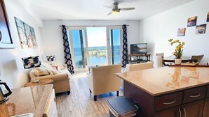 Una cocina moderna con una isla central, un comedor con mesa y sillas, y una sala de estar con sofá y televisor.