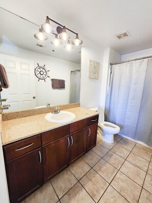A bathroom with a sink, vanity, mirror, and toilet. There is a shower curtain and a towel hanging on the wall.