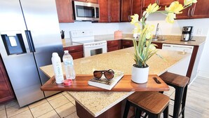 Una cocina moderna con armarios de madera, electrodomésticos de acero inoxidable, encimera de granito y una isla central con taburetes de bar.