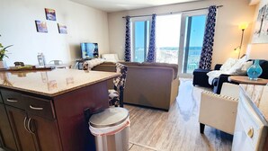 A modern kitchen with a central island, a dining area with a sofa, and a view of the city through large windows. - Next to 10th Floor Pool, incredible views! Light Show From Balcony! (Panama City Beach)