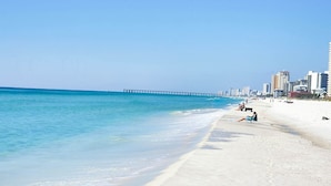 A beach with a clear blue sky, a sandy shore, and a pier extending into the water. - Gorgeous Set up! Dive into the best vacation with Best Amenities! (Panama City Beach)