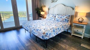 A bedroom with a bed, bedside tables, a ceiling fan, a view of the outdoors, and a large window. - Gorgeous Set up! Dive into the best vacation with Best Amenities! (Panama City Beach)