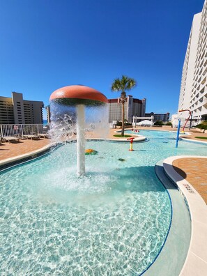 Une piscine agrémentée d’un élément décoratif aquatique, entourée d’une terrasse et de palmiers.