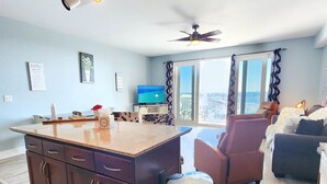 Un vaste espace de vie comprenant un îlot de cuisine, un ventilateur de plafond et une vue sur la ville grâce à de grandes fenêtres.