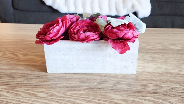 A wooden table with a white rectangular box containing red flowers. In the background, there is a dark-colored sofa with white and gray cushions. - On the most private end of the building, accessible and gorgeous! (Panama City Beach)