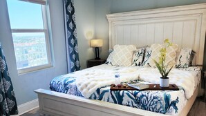 A bedroom with a large bed, a nightstand, a window with curtains, and a view of the outside. - On the most private end of the building, accessible and gorgeous! (Panama City Beach)