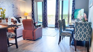 A spacious living room with a wooden floor, a ceiling fan, a sofa, a dining table with chairs, and large windows with curtains. - On the most private end of the building, accessible and gorgeous! (Panama City Beach)
