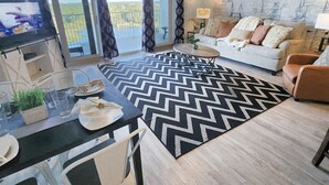 A modern living room with a large window, a ceiling fan, a dining area with a table and chairs, and a sofa with decorative pillows. - Immaculate! Large and inviting! Dive into the best vacation NOW! (Panama City Beach)