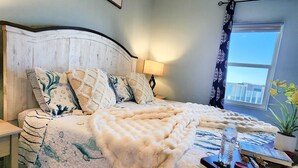 A bedroom with a bed, a nightstand, a lamp, a window with a view, and a ceiling fan. - Immaculate! Large and inviting! Dive into the best vacation NOW! (Panama City Beach)