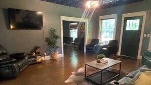 A modern living room with a leather sofa, a glass coffee table, and a large painting on the wall. There are two doors leading to other rooms, and a potted plant is visible.