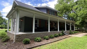 A two-story house with a covered porch, stone foundation, and a well-maintained lawn.