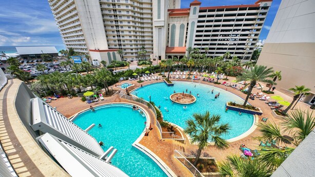 A large outdoor swimming pool with multiple sections, surrounded by palm trees and lounge chairs. - Best Location, 3rd floor condo! Enjoy the incredible views and privacy! (Panama City Beach)