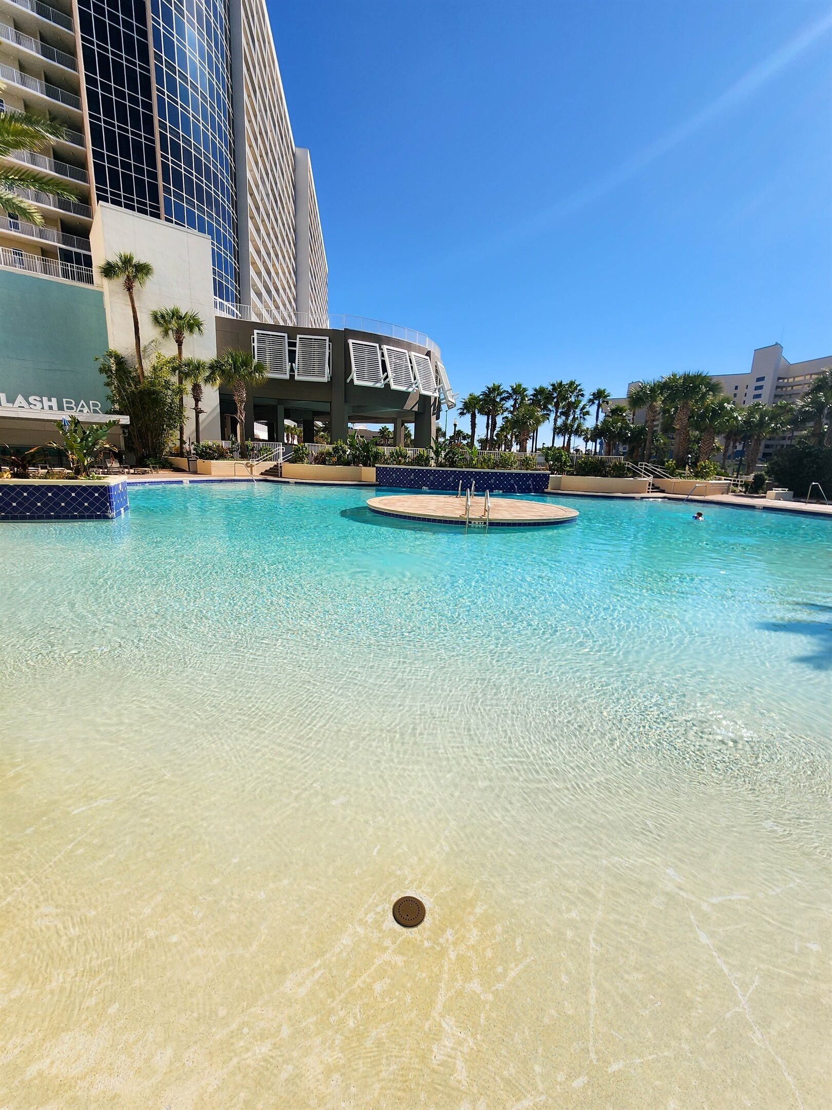 Una piscina con acqua cristallina, circondata da palme e da un edificio con balconi.