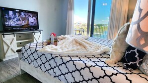 A bedroom with a bed, a TV, a ceiling fan, and a balcony with a view.