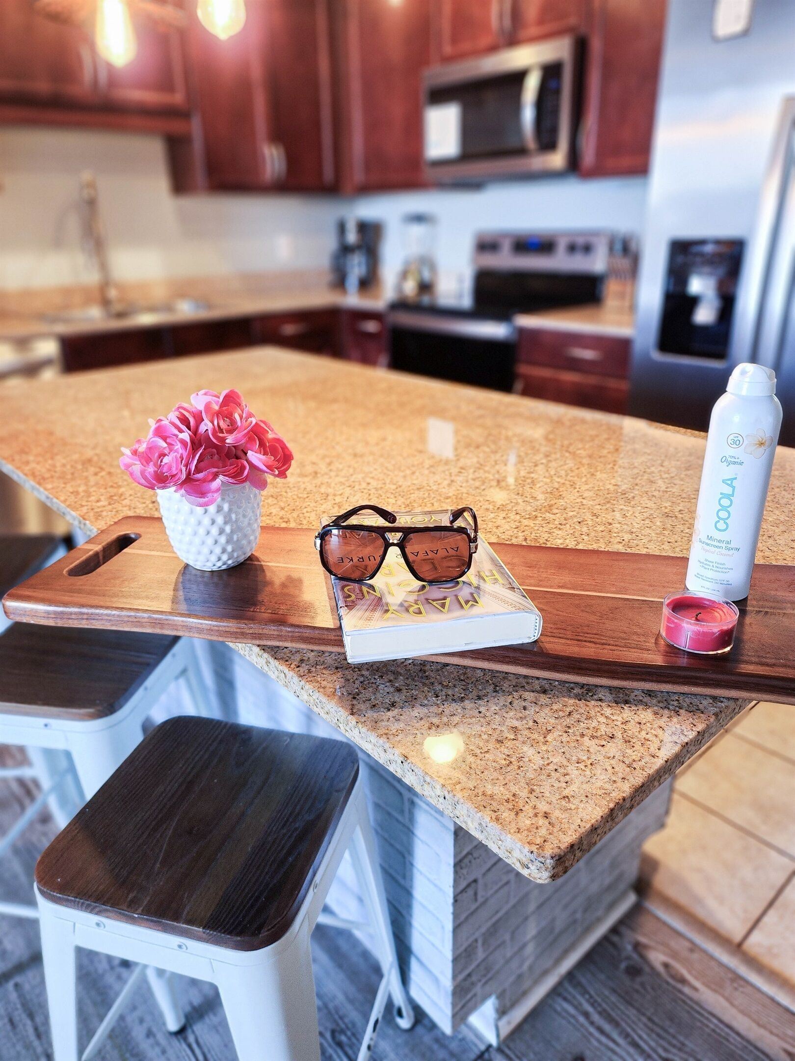 Un comptoir de cuisine avec un livre, une paire de lunettes de soleil, une bougie et une bouteille d’eau.