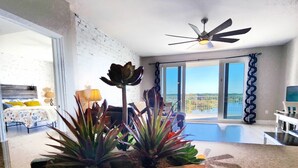 Amplia sala de estar con un ventanal grande, ventilador de techo y jardinera de madera con suculentas.