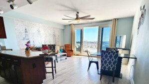 A spacious living area with a kitchen, a dining table, and a balcony with a view. - Perfect location on 5 FTH FLOOR! Amazing set up for a memorable stay! (Panama City Beach)