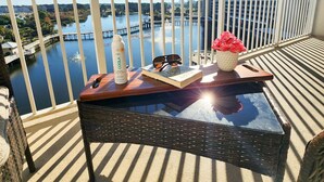A balcony with a view of a body of water, a wooden table with a bottle, glasses, and a book, and a potted plant. - Perfect location on 5 FTH FLOOR! Amazing set up for a memorable stay! (Panama City Beach)