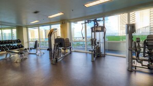 A gym with various exercise equipment, large windows, and a view of buildings outside.