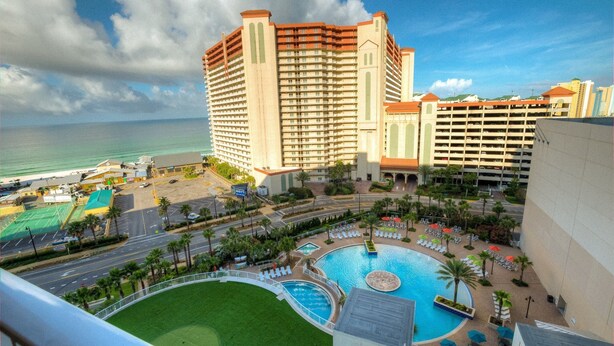 A hotel with a large pool, a tennis court, and a view of the ocean.