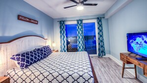 A bedroom with a bed, a ceiling fan, a TV, and a window with curtains.