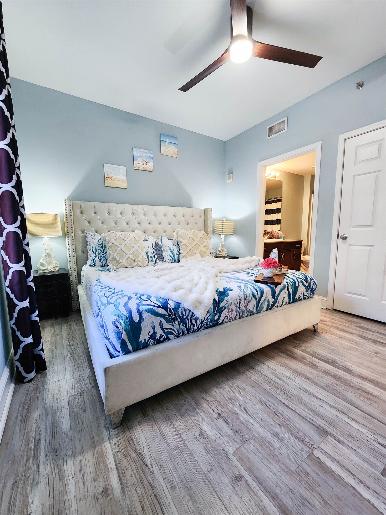 Un dormitorio con una cama grande, un ventilador de techo y una puerta que da a un baño.