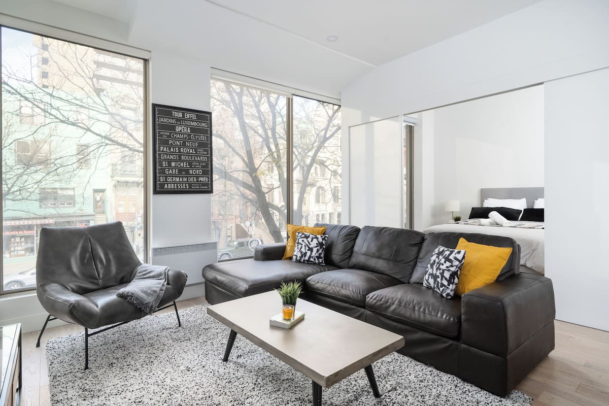 A modern living room with a leather sofa, a coffee table, and a large window with a city view.