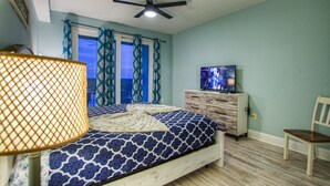 Un dormitorio con cama, ventilador de techo, televisor, cómoda y una silla.