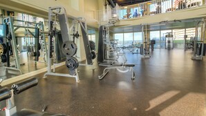 Un gimnasio amplio con diversos equipos de ejercicio, un entrepiso y ventanas grandes.