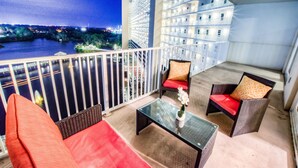 Un balcón con mobiliario de mimbre, una mesa de vidrio y vistas a un paisaje urbano nocturno.