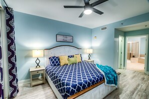 Ein Schlafzimmer mit einem Bett, zwei Nachttischen, einem Deckenventilator und einer Tür zu einem anderen Raum.