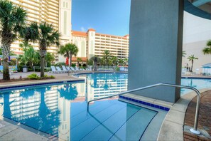 Ein Hotelpool mit klarem, blauem Wasser, Palmen und einem großen Gebäude im Hintergrund.