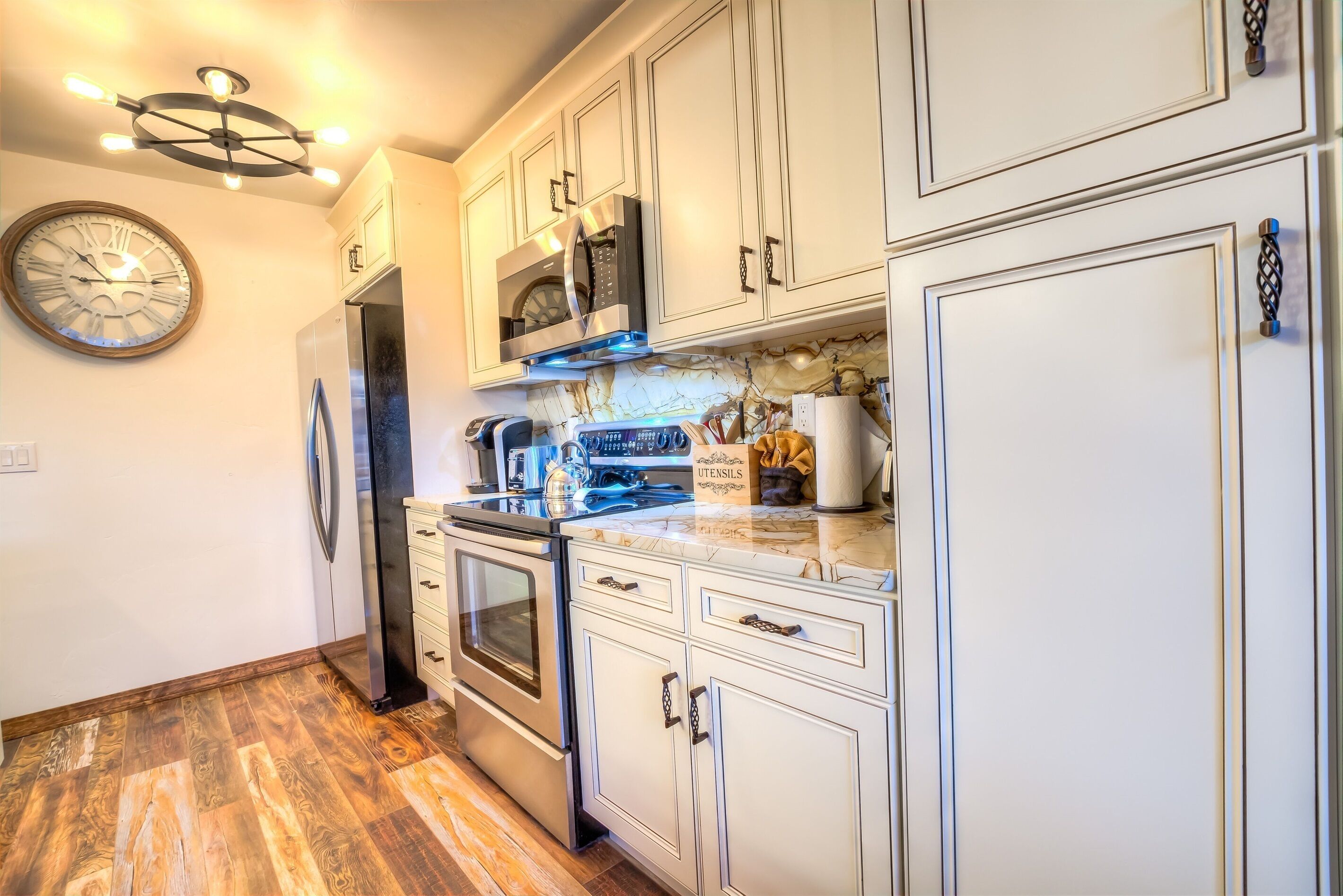 A modern kitchen with white cabinetry, stainless steel appliances, and a wooden floor.