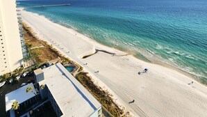 Ein Strand mit klarem, blauem Wasser, einer langen Seebrücke und einem Gebäude mit Balkonen mit Blick auf den Strand.