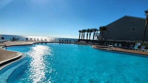 Ein klarblauer Pool mit geschwungener Kante, umgeben von Liegestühlen und Palmen, in der hellen Sonne.