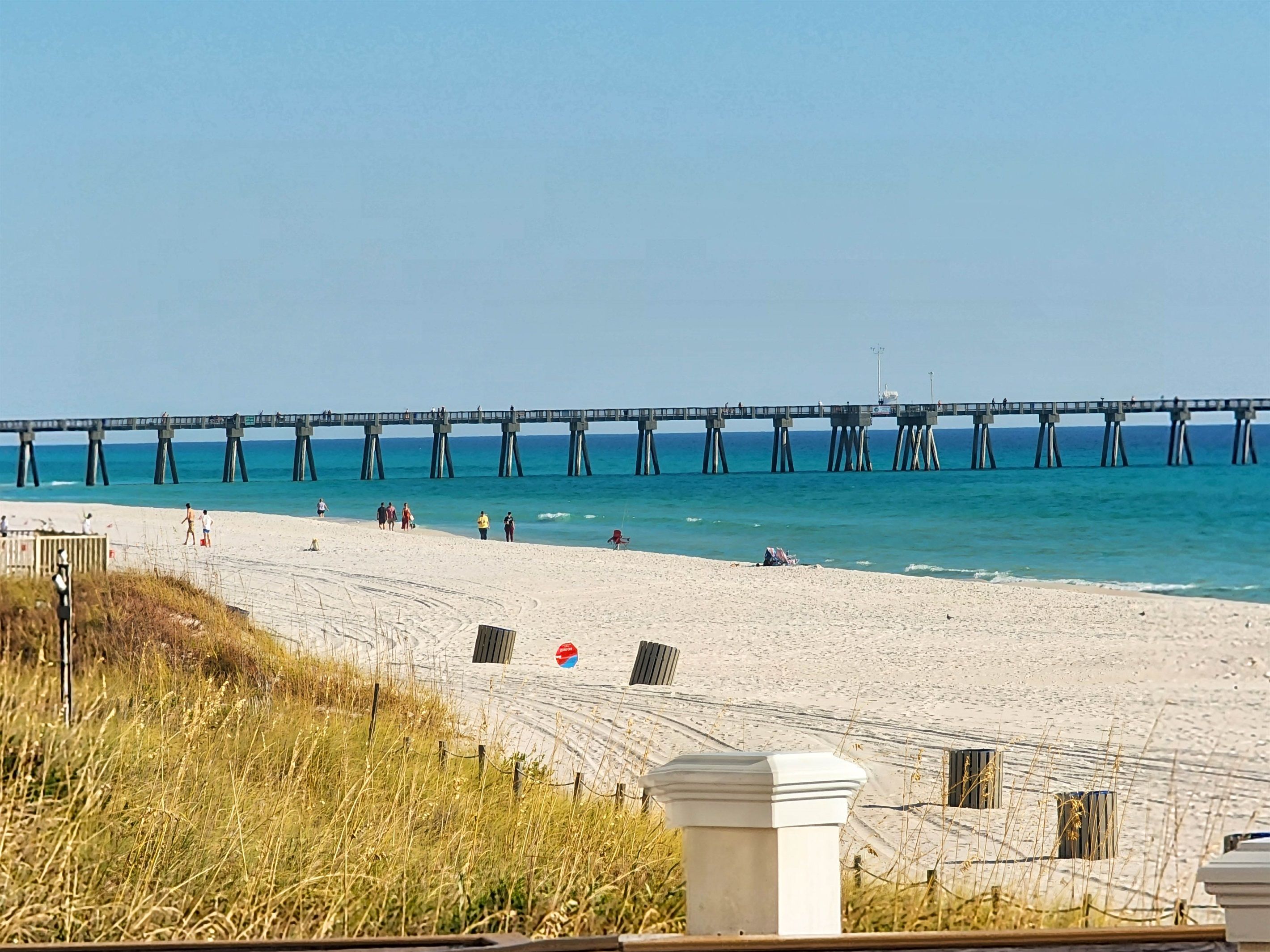 A beach with a pier extending into the ocean, sandy beach, and a no swimming sign.