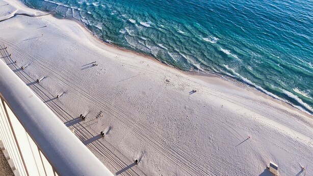 Ein Strand mit klarem, blauem Wasser und einer langen Mole, die sich ins Meer erstreckt.