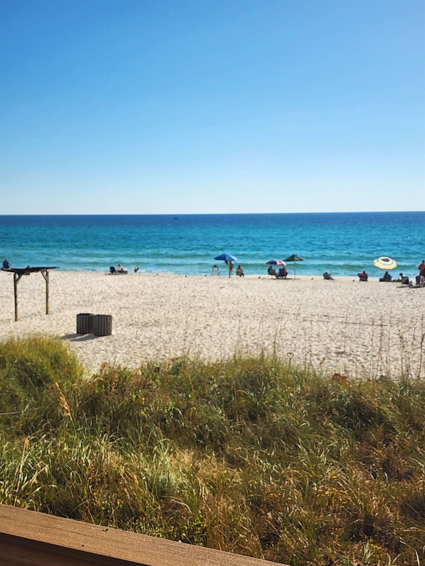 Une plage où les gens se détendent et prennent des bains de soleil, un ciel dégagé et une mer calme.