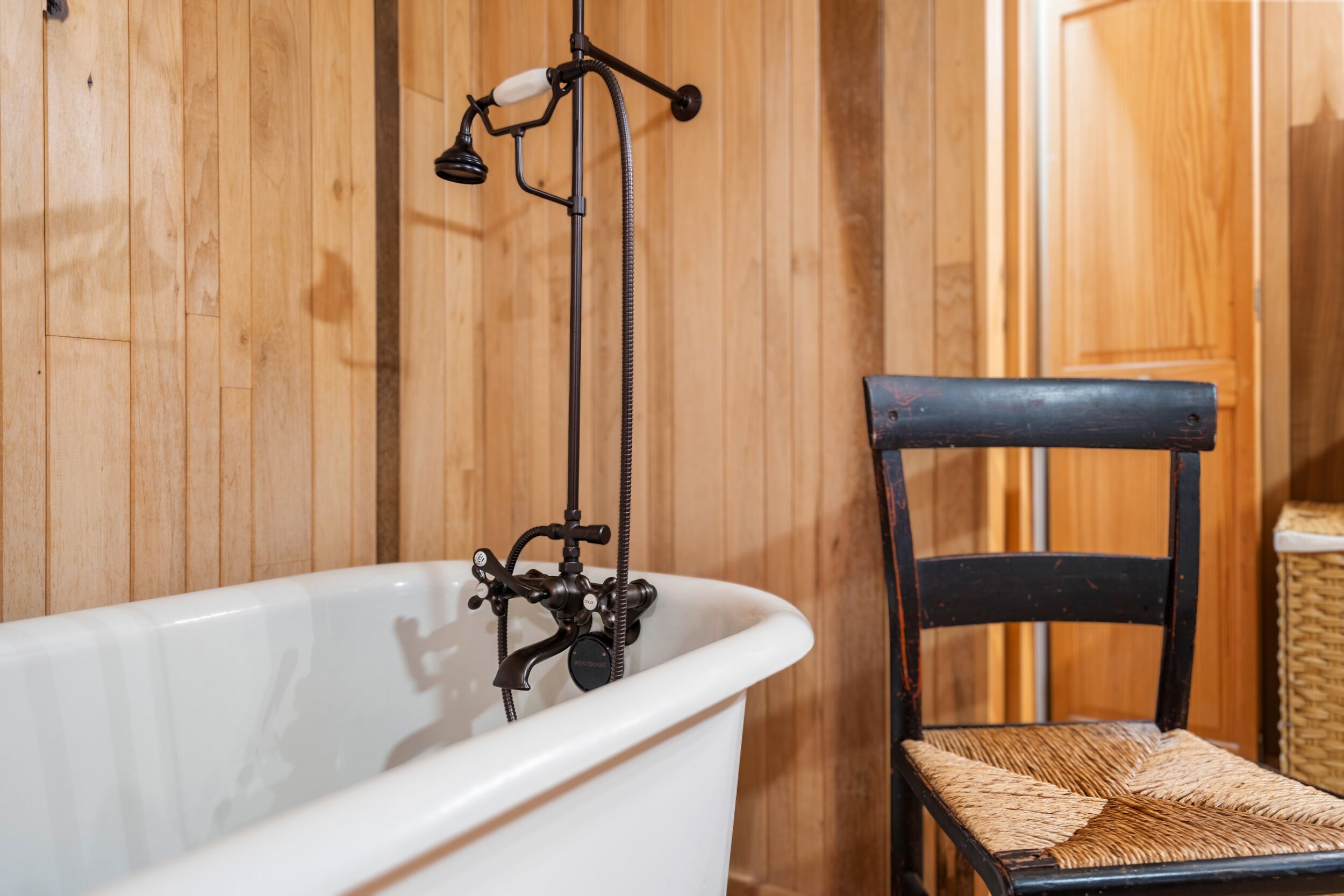 Une baignoire avec un robinet d’époque et une chaise en osier placée à côté.