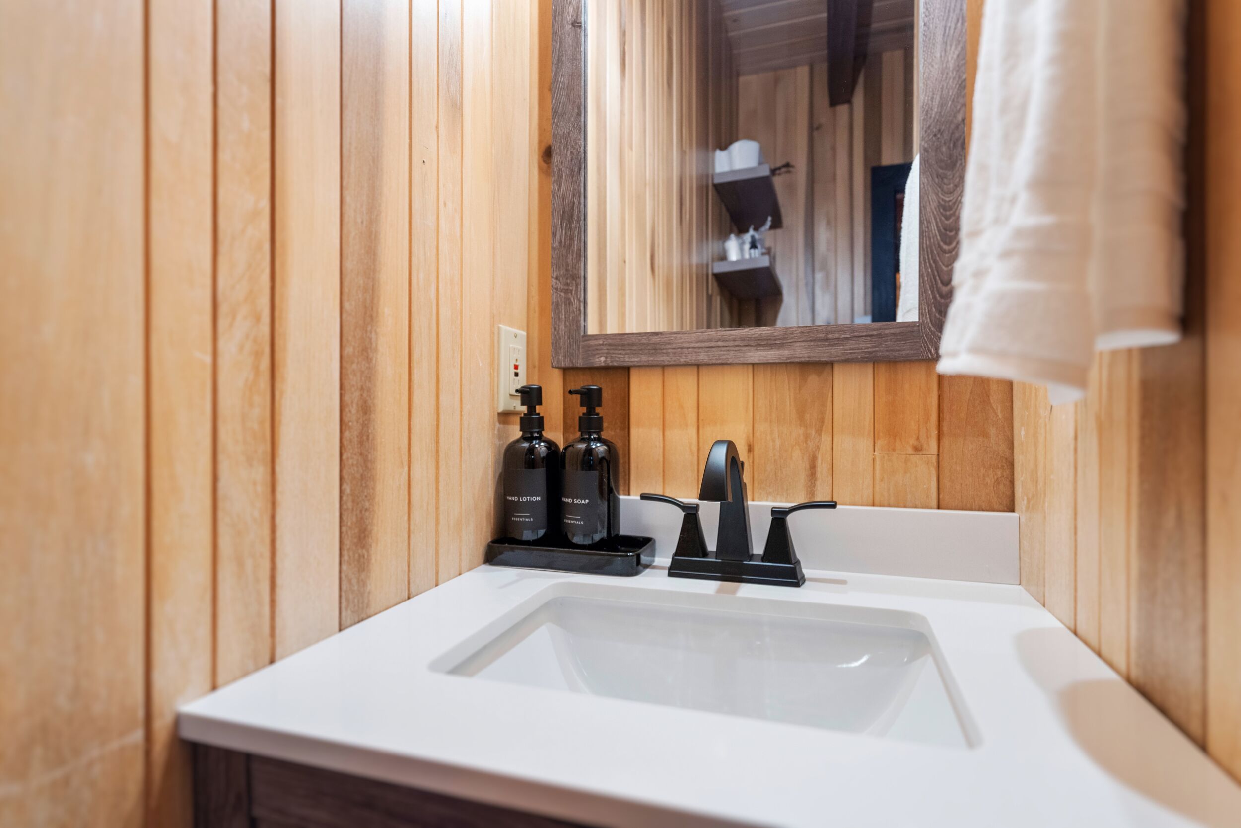 Une salle de bain avec des murs recouverts de panneaux en bois, un lavabo blanc et deux distributeurs de savon noirs.