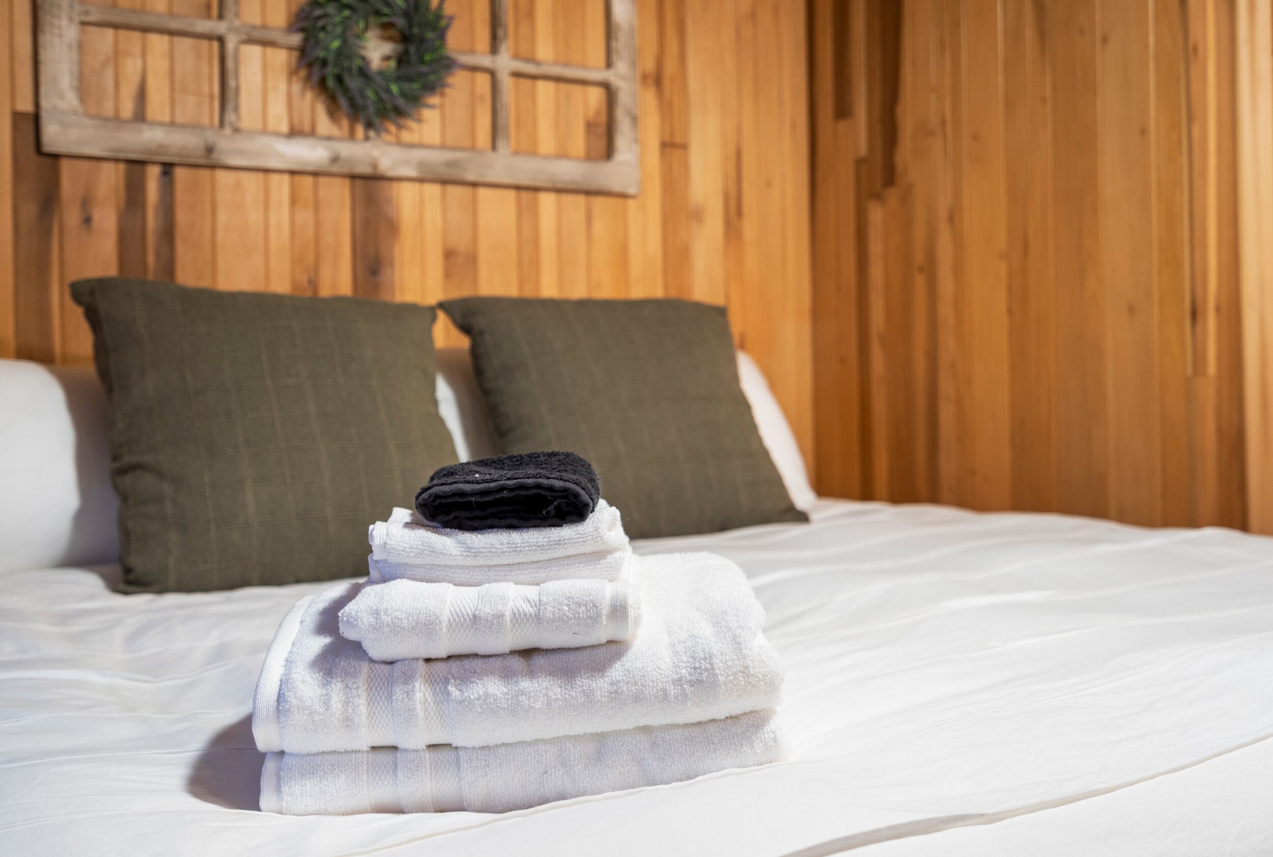 A neatly made bed with white linens and a stack of folded towels in front.