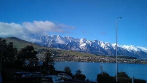 A lake with mountains in the background, a parking area with cars, and a clear sky.