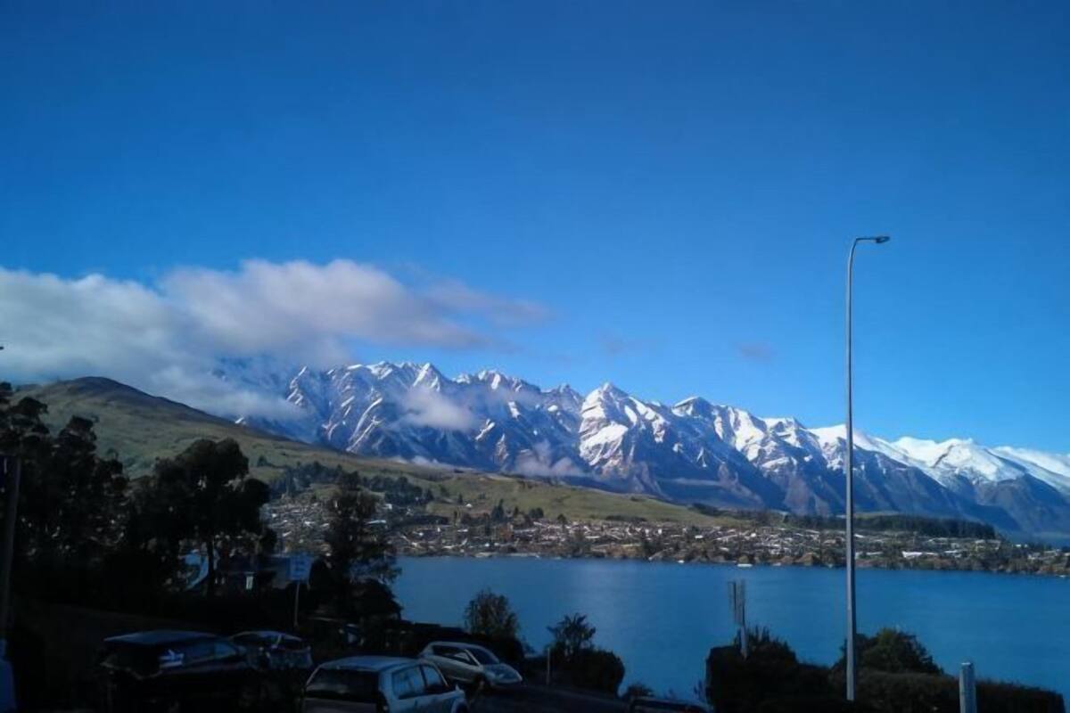 Un lago con montañas al fondo, un estacionamiento con coches y un cielo despejado.