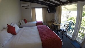 A hotel room with two beds, a small table, chairs, and a balcony with a view.